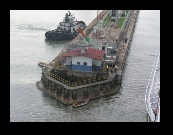 Out on the end of the concrete pier, the mechanical indicator arrow points us to the right side lock. The men in the small boat will catch lines thrown from the ship and attach them to the little train called a "mule".